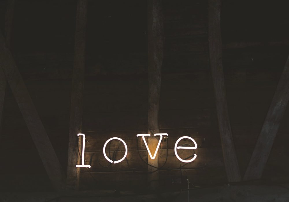 The word love in warm neon against the dark boards of a barn wall