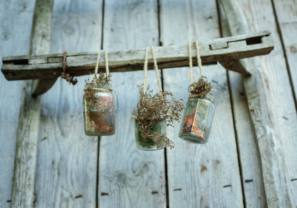 Jam jars of gypsophila hanging from a ladder against a painted plank wall